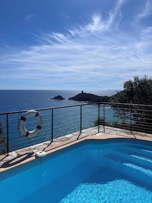 Una piscina con un flotador salvavidas, cielo despejado y una vista distante del mar y las islas.