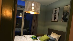 Un dormitorio con una cama, almohadas, una lámpara colgante y dos cuadros en la pared.