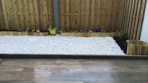 Un jardín con cercado de madera, piedras y macizos de flores.