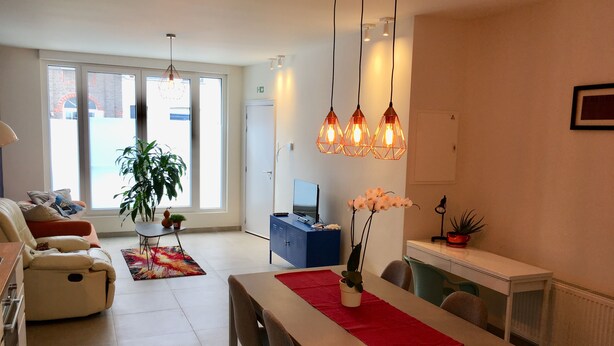 Una sala de estar moderna con un sofá, una mesa de comedor con sillas, un televisor y un ventanal con vistas.