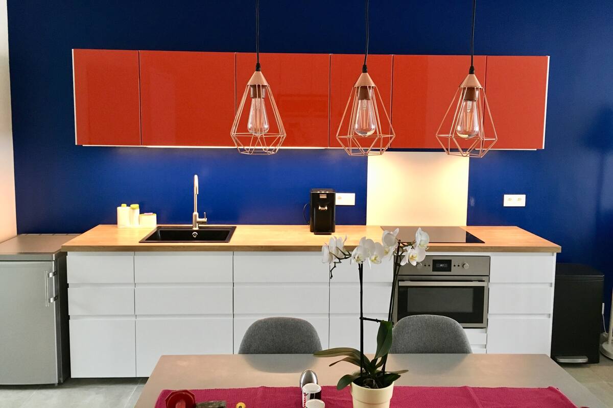 A modern kitchen with red cabinets, a sink, and a dining area with a table and chairs.