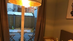 Habitación de hotel con cama, mesita de noche, lámpara y vista al balcón exterior.
