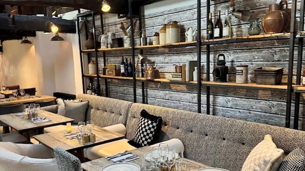 Um restaurante acolhedor com vigas de madeira, um sofá e mesas preparadas para refeições.