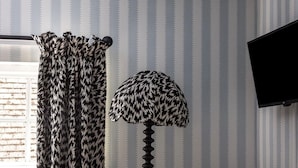 Um quarto com papel de parede listrado, uma cortina com estampa de leopardo, piso estampado, uma poltrona listrada e um abajur alto.