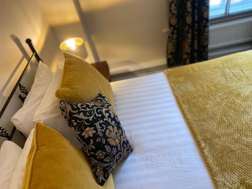A bed with a white mattress, a yellow blanket, and two pillows, one yellow and one with a black floral pattern.