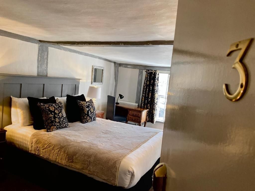 Habitación de hotel con una cama grande, un escritorio y una silla. Hay una ventana con cortinas y el número 3 en la pared.