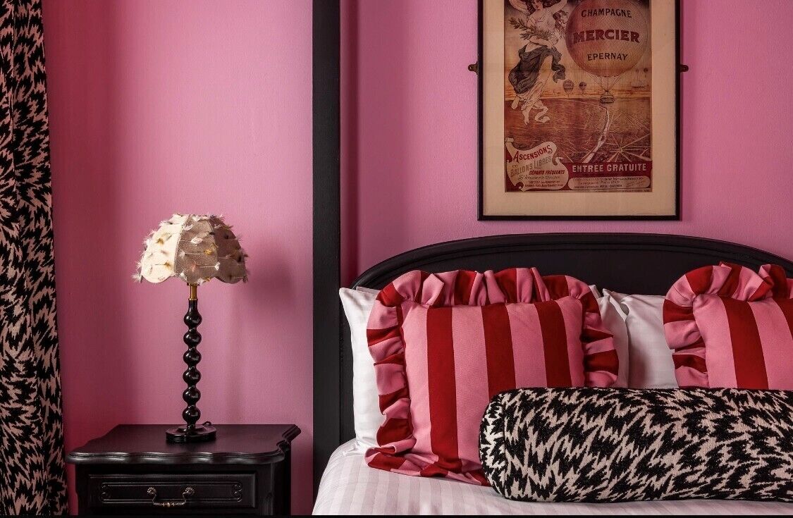 A bedroom with a bed, pillows, a nightstand, a lamp, and a framed poster on the wall.