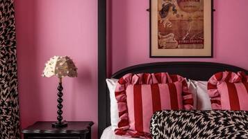 A bedroom with a bed, pillows, a nightstand, a lamp, and a framed poster on the wall.