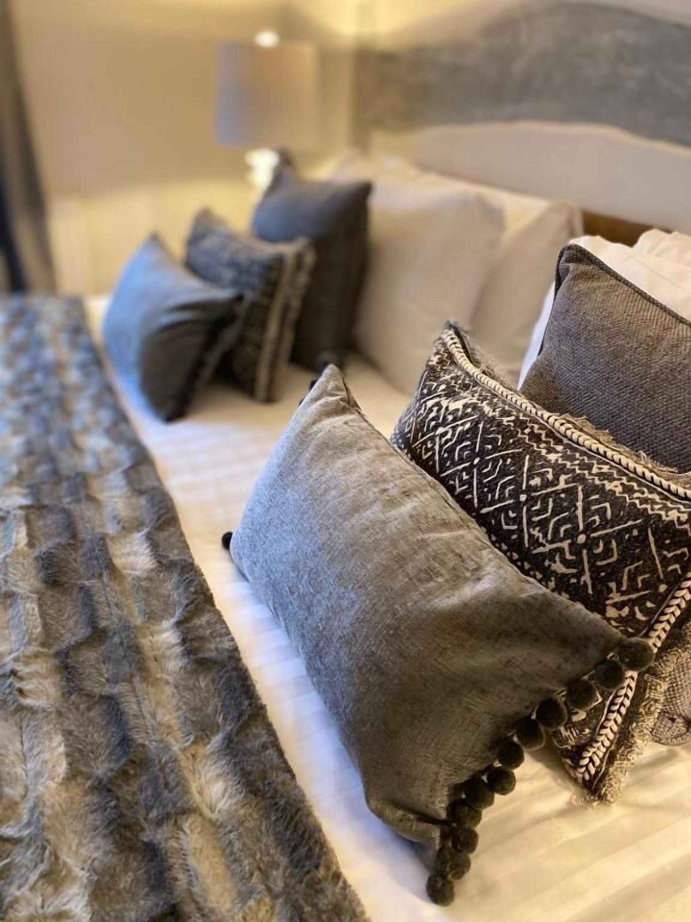 Ein Bett mit grauen und gemusterten Kissen, einer strukturierten Decke und einer Nachttischlampe.