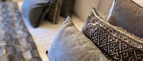 A bed with grey and patterned pillows, a textured blanket, and a bedside lamp.