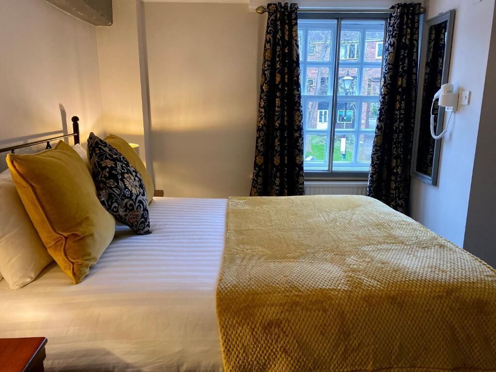 A hotel room with a bed, a bedside table, a window with curtains, and a wall-mounted phone.