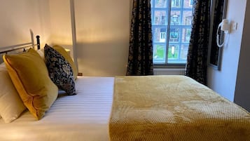 A hotel room with a bed, a bedside table, a window with curtains, and a wall-mounted phone.