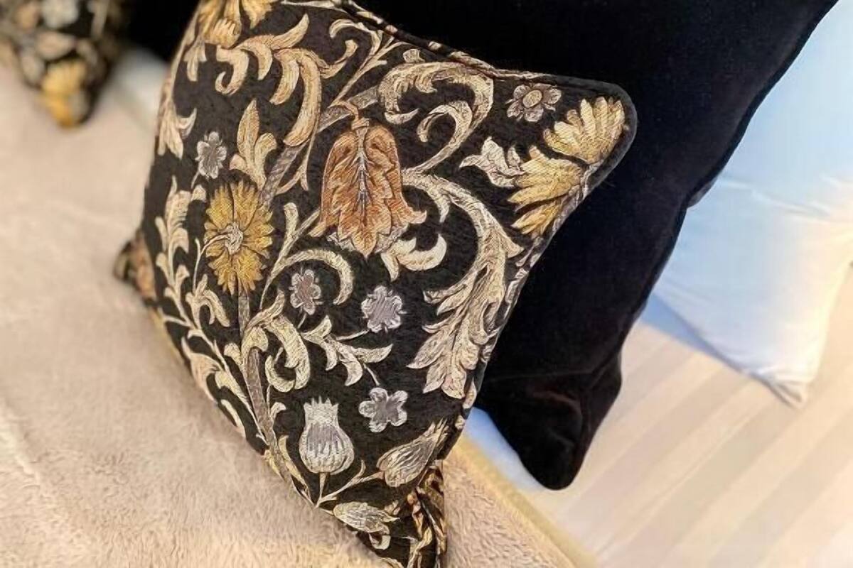 Una cama con ropa blanca y almohadas negras con bordados dorados.