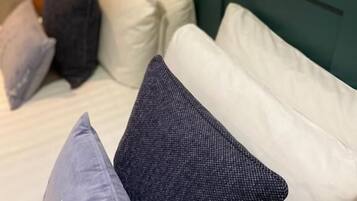 Una cama con cabecera verde y varios almohadones de distintos colores.