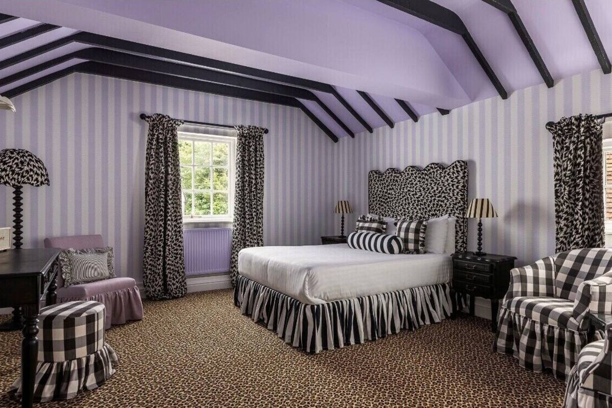 Un dormitorio con papel tapiz a rayas, una cama con colcha de cuadros blancos y negros, un cabecero con diseño blanco y negro, y una alfombra de estampado de leopardo.