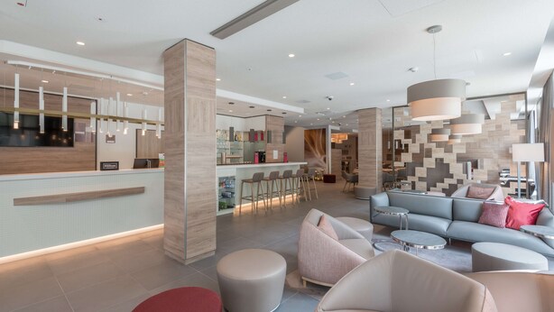 A modern hotel lobby with a reception desk, seating area, and a bar. - Hampton by Hilton Frankfurt City Centre East (Frankfurt)