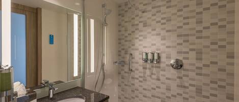 Un bagno moderno con cabina doccia in vetro, uno specchio grande e un lavabo su un piano in granito.