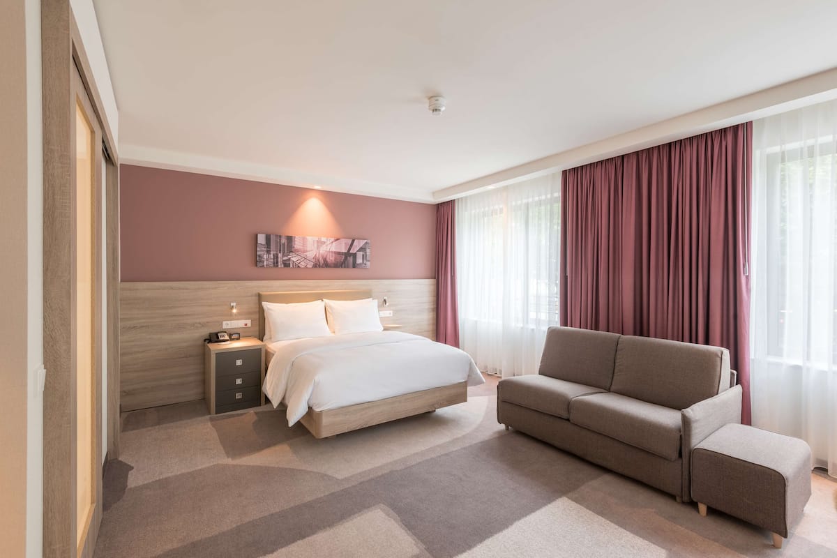 Ett hotellrum med en säng, en soffa, ett sängbord och ett konstverk som hänger på väggen.