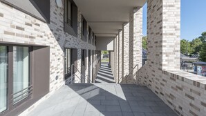 A covered outdoor corridor with a brick wall, metal railings, and a tiled floor. - Hampton by Hilton Frankfurt City Centre East (Frankfurt)
