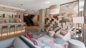 A modern hotel lobby with a bar area, seating arrangements, and a staircase. - Hampton by Hilton Frankfurt City Centre East (Frankfurt)