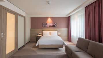 A modern hotel room with a large bed, a sofa, a nightstand, and a wall-mounted artwork.