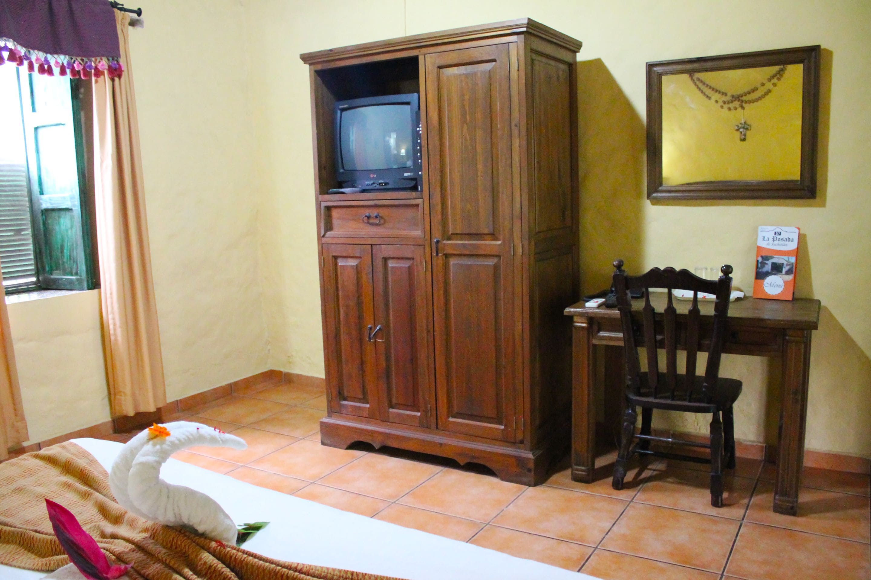 A room with a wooden cabinet containing a television, a wooden chair, and a framed picture on the wall.