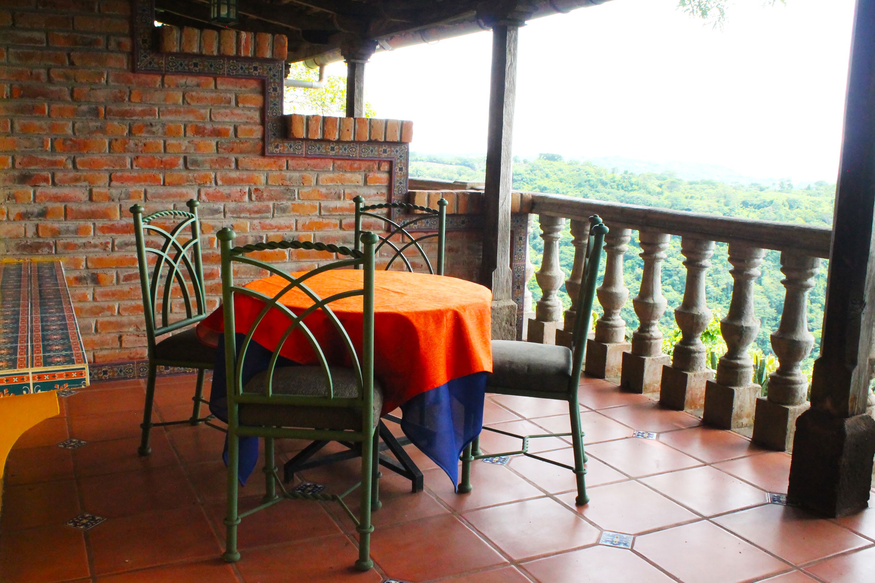 A terrace with a brick wall, a table with a tablecloth, and a view of greenery.