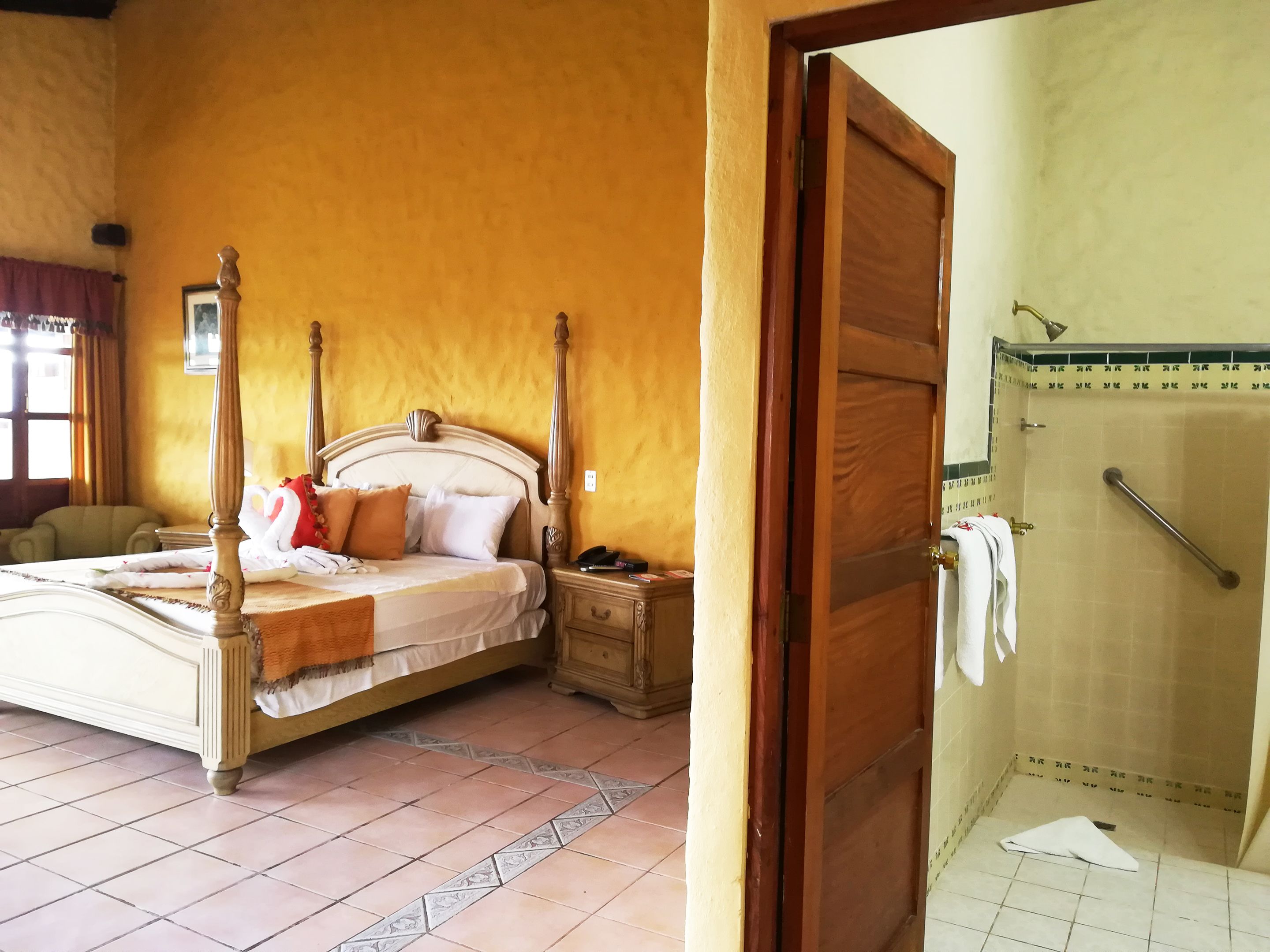 A bedroom with a four-poster bed, a nightstand, and a bathroom with a shower.