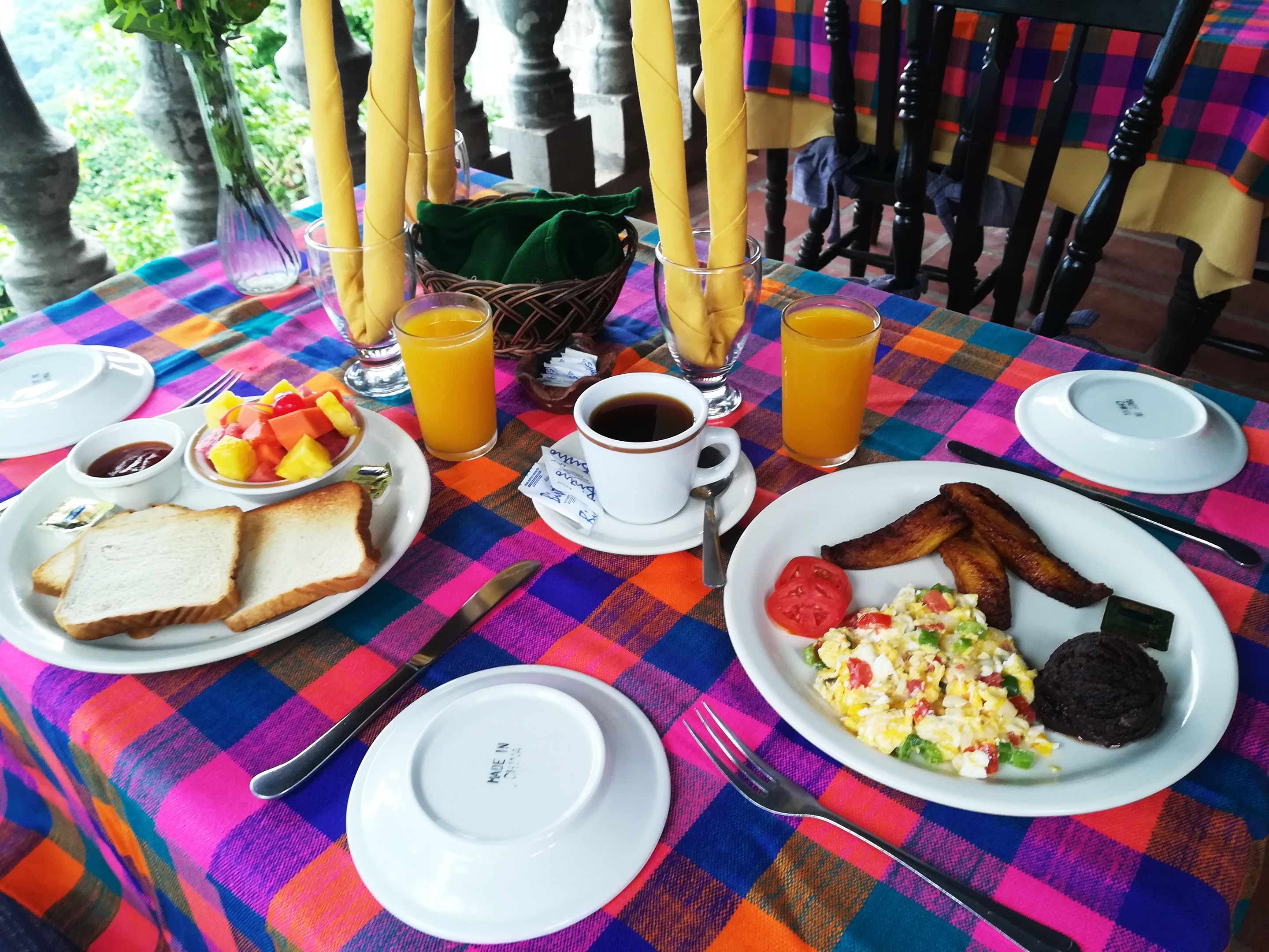 A breakfast table with plates of toast, eggs, bacon, and fruit, along with cups of coffee and orange juice.