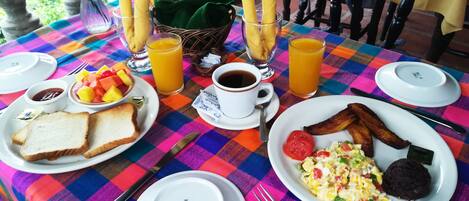 A breakfast table with plates of toast, eggs, bacon, and fruit, along with cups of coffee and orange juice.