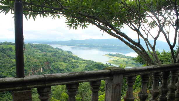 A scenic view from a balcony overlooking a lush valley and a large body of water.