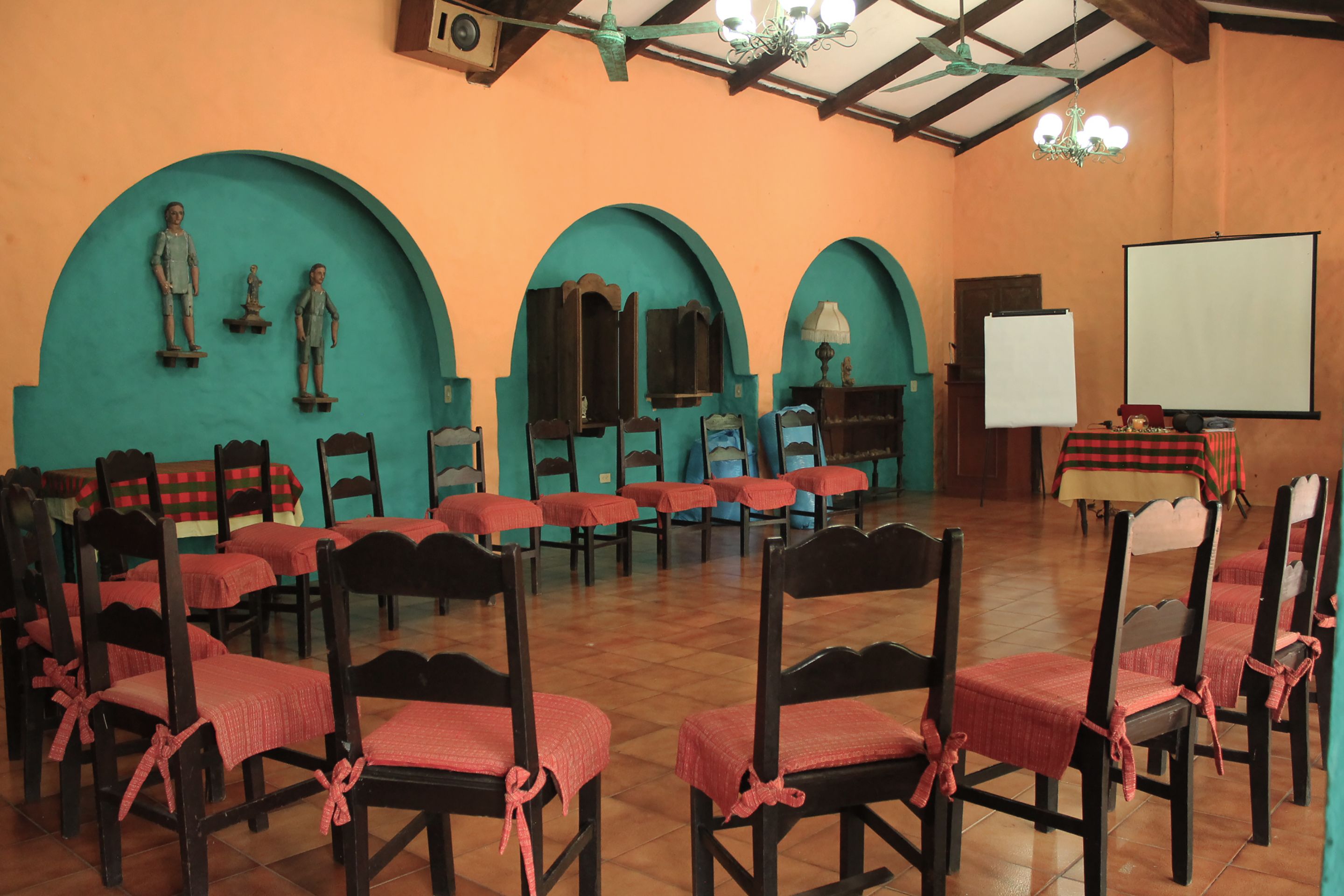 A conference room with wooden chairs and tables, a whiteboard, and a projector screen.