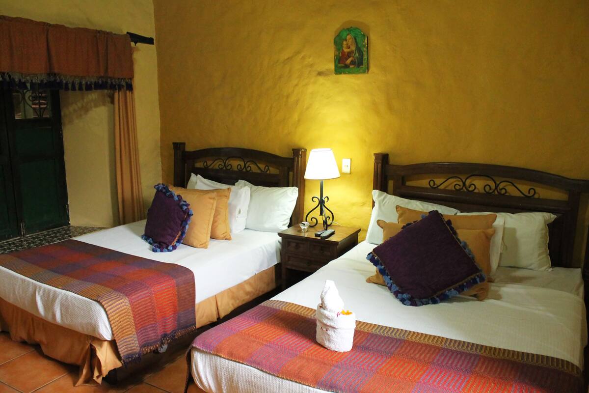 A hotel room with two beds, each with a plaid bedspread, a nightstand with a lamp, and a wall-mounted picture.