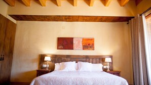 A hotel room with a large bed, wooden headboard, two bedside tables with lamps, a painting on the wall, and a window with curtains. - Mas del Bot (Valderrobres)
