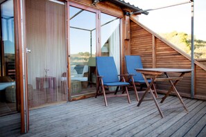 A wooden deck with two blue chairs and a table, a sliding glass door, and a view of the landscape.