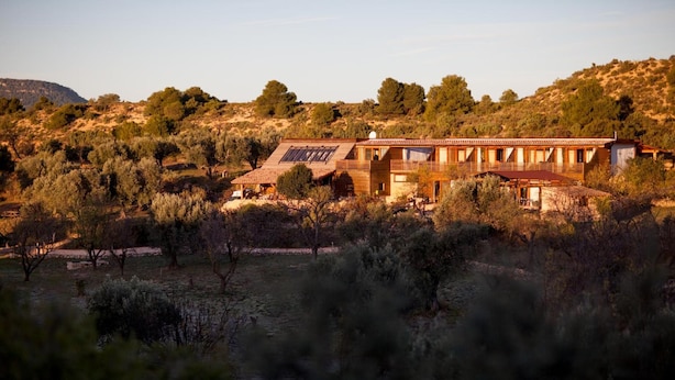 A modern house with a flat roof, large windows, and solar panels, surrounded by a dry, hilly landscape with sparse vegetation. - Mas del Bot (Valderrobres)