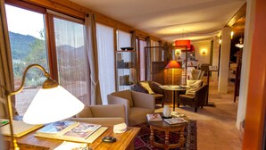 A cozy hotel room with a wooden desk, a comfortable sofa, a small round table, and a view of the outdoors through large windows. - Mas del Bot (Valderrobres)