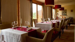 A dining area with multiple tables set for a meal, featuring red pendant lights and a view of the outdoors through large windows. - Mas del Bot (Valderrobres)