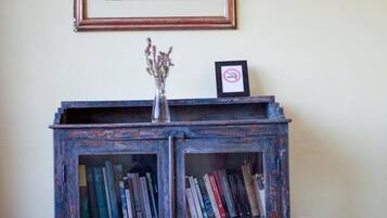 Uma estante de madeira rústica com livros e um vaso de flores, um quadro na parede e uma poltrona xadrez em primeiro plano.