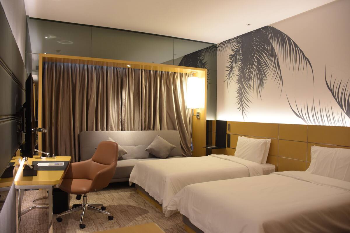 Habitación de hotel con dos camas, un escritorio con silla, televisión y un mural grande en la pared.