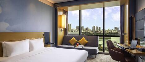 Une chambre d’hôtel avec un lit, un canapé, un bureau avec un ordinateur portable et une vue sur le paysage urbain.