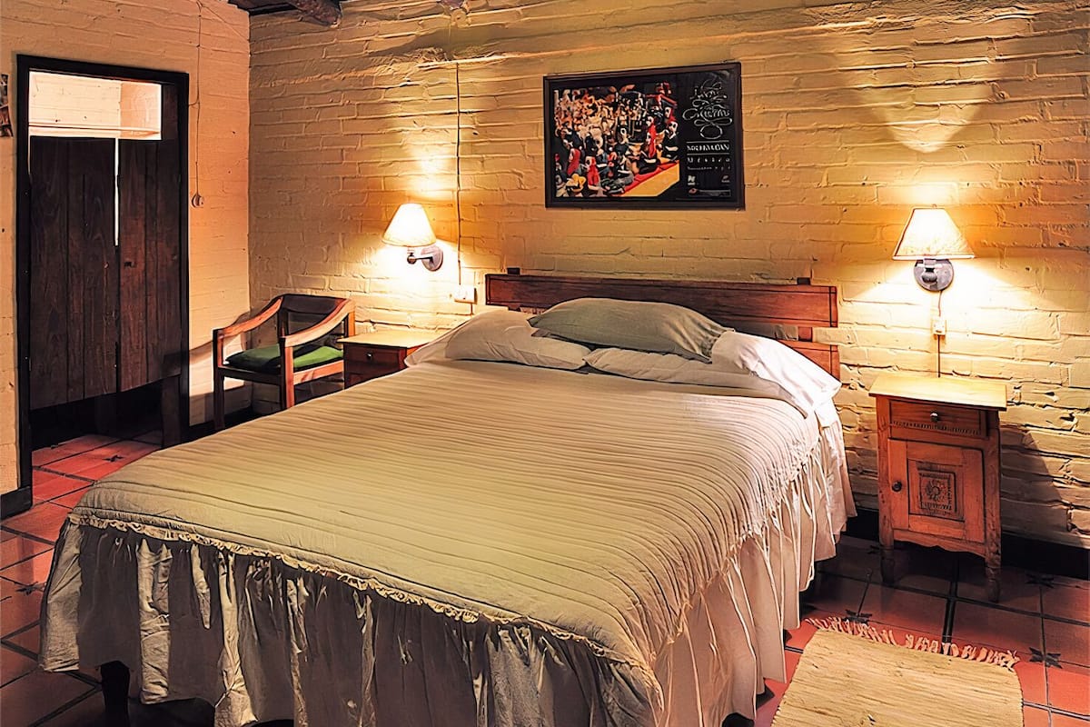 A cozy room with a bed, two chairs, a wooden cabinet, and a wall-mounted picture.