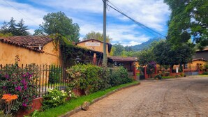 Un hotel rústic amb teulada d'àmples rajoles, envoltat de vegetació exuberànt i un carrer empedrat.