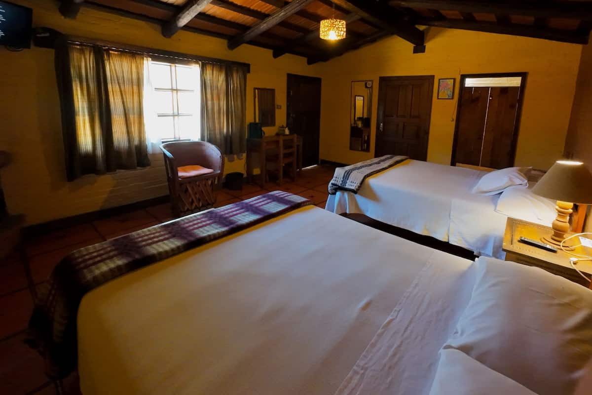 A hotel room with two beds, a chair, a desk, and a lamp.