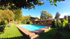 Una piscina envoltada d'un jardí ben cuidat, amb una casa al fons.