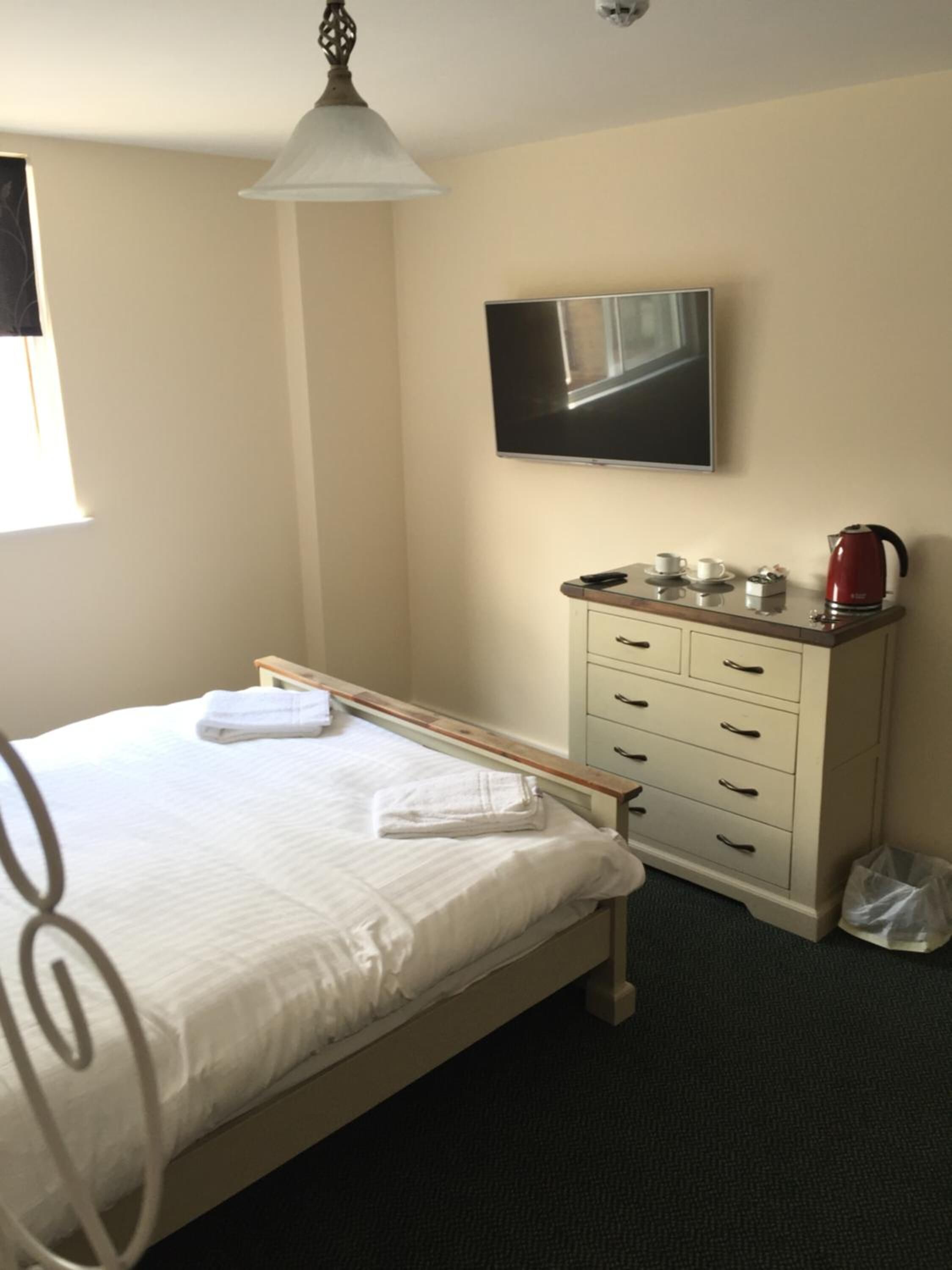 A hotel room with a bed, a bedside table with a kettle, a TV, and a window.