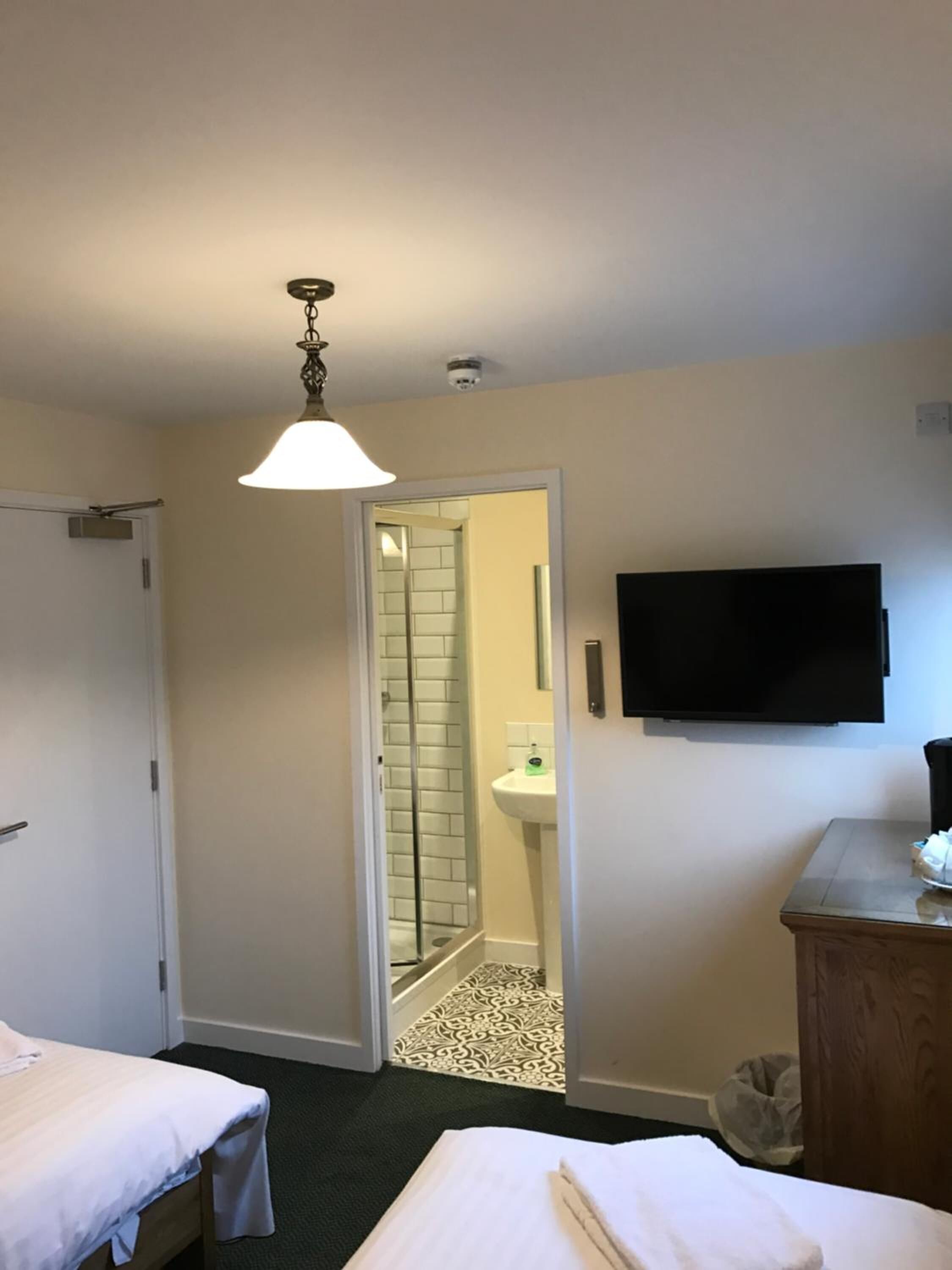 A hotel room with two beds, a TV, a bathroom with a shower, and a ceiling light.