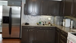 Eine Küche mit dunklen Holzausbau, einem Edelstahlkühlschrank, einer gemusterten Spritzschutzwand und einer Arbeitsplatte mit Spüle und verschiedenen Geräten.