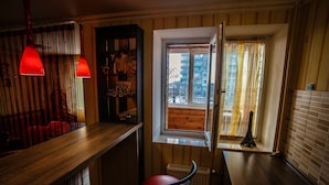 Une pièce avec un comptoir en bois, une chaise rouge, une fenêtre donnant sur des immeubles et un radiateur.