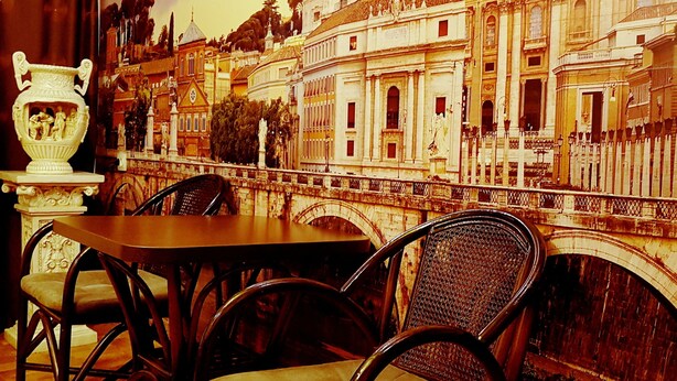 Un espace repas comprenant une table et des chaises, un vase décoratif et une fresque représentant un bâtiment historique.